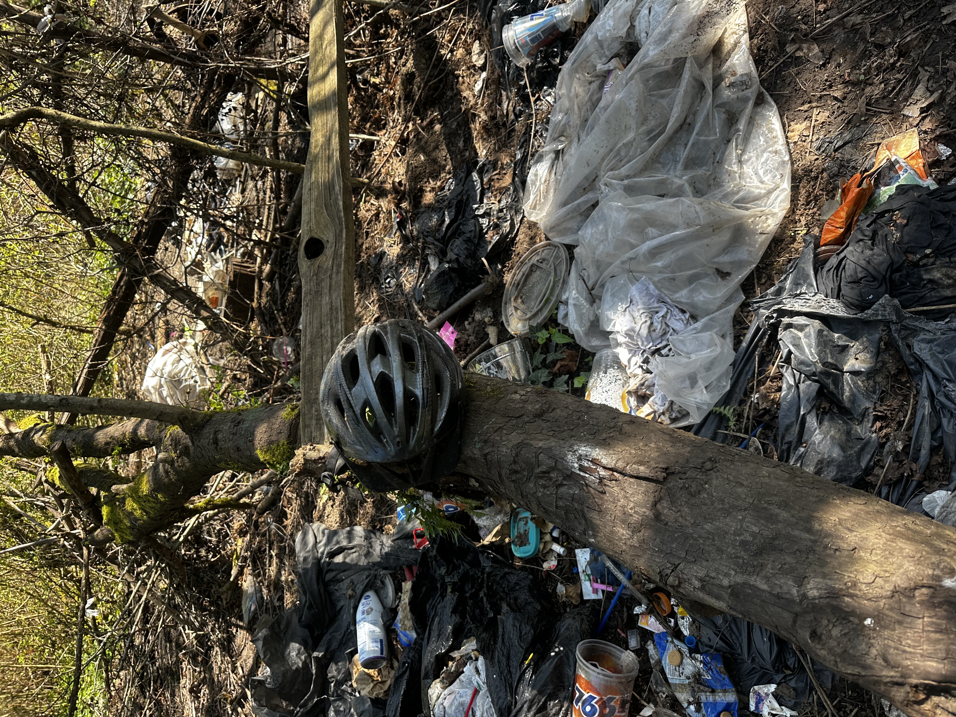 Debris pile with discarded items including helmet, plastic sheeting, and garbage bags
